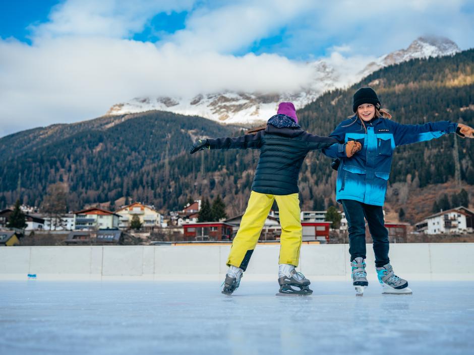 Sie sehen zwei Kinder beim Eislaufen am Eislaufplatz