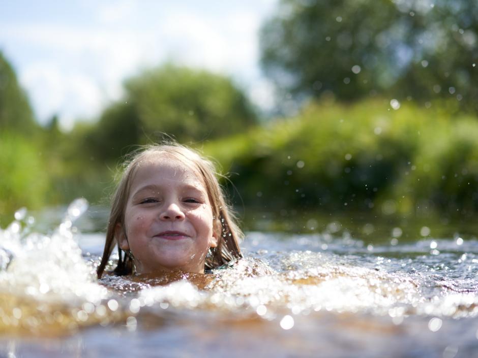 Sie sehen ein lachendes Kind beim Schwimmen in einem See in der Nähe von JUFA Hotels.