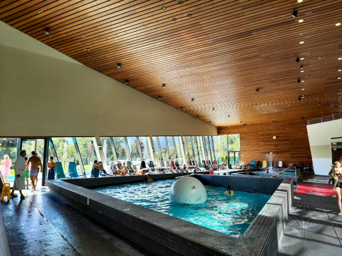 Sie sehen ein Schwimmbecken und die wunderschöne Holzdeckein der Aqualux Therme. JUFA Hotels bietet tollen Urlaub mit viel Abenteuer und Spaß für die ganze Familie.