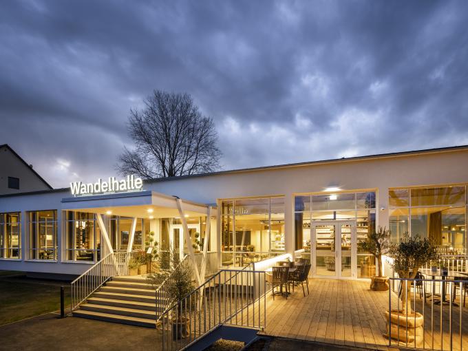 Sie sehen eine Außenansicht in der Abendstimmung des Café & Restaurant Wandelhalle im JUFA Hotel Bad Radkersburg mit großer Terrasse im Kurpark Bad Radkersburg.