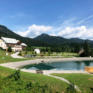 Sie sehen das JUFA Hotel Gitschtal Landerlebnis mit Bergsee und Landschaft. JUFA Hotels bietet kinderfreundlichen und erlebnisreichen Urlaub für die ganze Familie.