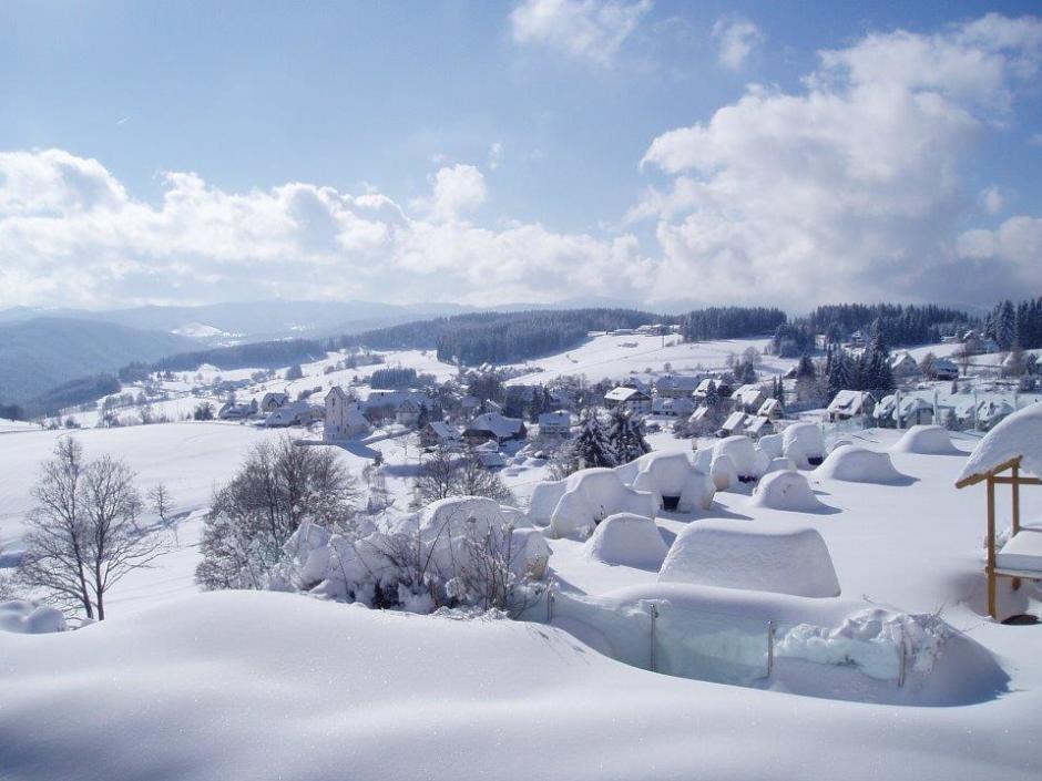 Sie sehen eine verschneite Winterlandschaft, den Ort Saig mit Bergen im Hintergrund vom JUFA Hotel Schwarzwald***s aus.