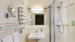 Sie sehen ein Badezimmer mit Waschbecken und Dusche  im JUFA Hotel Graz City***. Der Ort für erlebnisreichen Städtetrip für die ganze Familie und der ideale Platz für Ihr Seminar.