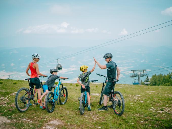 Sie sehen eine Familie bestehend aus zwei Erwachsenen und zwei kleinen Kindern mit ihren Mountainbikes auf der Petzen.