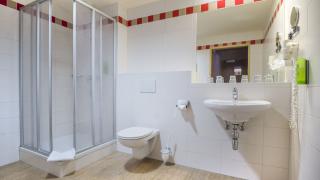 Sie sehen ein Badezimmer im JUFA Hotel Altenmarkt*** mit WC, Dusche und Waschbecken.