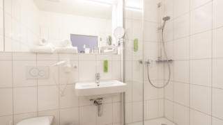 Sie sehen ein Badezimmer im JUFA Hotel Bregenz mit Dusche. JUFA Hotels bietet erlebnisreichen Städtetrip für die ganze Familie und den idealen Platz für Ihr Seminar.