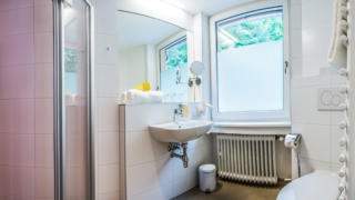 Sie sehen ein Badezimmer im JUFA Hotel Königswinter/Bonn mit Dusche und WC. JUFA Hotels bietet erlebnisreichen Städtetrip für die ganze Familie und den idealen Platz für Ihr Seminar.