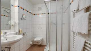 Sie sehen ein Badezimmer im JUFA Hotel Veitsch mit Dusche. JUFA Hotels bietet kinderfreundlichen und erlebnisreichen Urlaub für die ganze Familie.