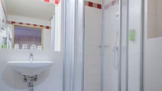Sie sehen ein Badezimmer im JUFA Hotel Altenmarkt*** mit Waschbecken, Dusche und WC.