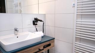 Sie sehen ein Waschbecken mit Ablageflächen sowie einen Föhn in einem Badezimmer im neuen JUFA Hotel Bad Radkersburg mit 4-Sterne-Komfort.