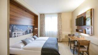 Sie sehen ein Bett mit Decke im Doppelzimmer im JUFA Hotel Graz City***. Der Ort für erlebnisreichen Städtetrip für die ganze Familie und der ideale Platz für Ihr Seminar.