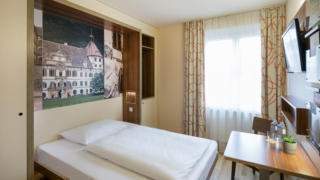 Sie sehen ein Bett mit Decke im Einzelzimmer im JUFA Hotel Graz City***. Der Ort für erlebnisreichen Städtetrip für die ganze Familie und der ideale Platz für Ihr Seminar.
