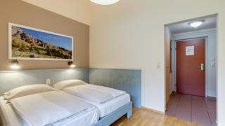 Doppelbett im Doppelzimmer im JUFA Hotel Veitsch mit Blick auf den Vorraum. JUFA Hotels bietet kinderfreundlichen und erlebnisreichen Urlaub für die ganze Familie.