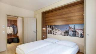 Sie sehen ein Bett vor einem Wandbild im Doppelzimmer im JUFA Hotel Graz City***. Der Ort für erlebnisreichen Städtetrip für die ganze Familie und der ideale Platz für Ihr Seminar.