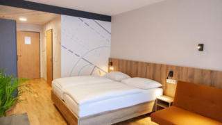 Sie sehen ein Doppelbett im Doppelzimmer/Familienzimmer FF3 im JUFA Hotel Mariazell – Erlaufsee Sport-Resort. Der Ort für erfolgreiches Training in ungezwungener Atmosphäre für Vereine und Teams.