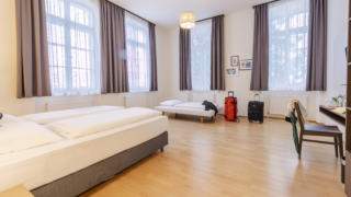 Sie sehen Betten in einem Familienzimmer Typ Family & Friends 3 im JUFA Hotel Bregenz mit einer Tasche. JUFA Hotels bietet erlebnisreichen Städtetrip für die ganze Familie und den idealen Platz für Ihr Seminar.