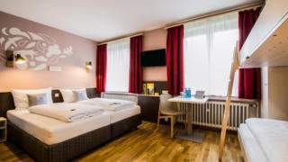 Sie sehen Betten im Familienzimmer Typ Family and Friends 4 im JUFA Hotel Königswinter/Bonn mit TV. JUFA Hotels bietet erlebnisreichen Städtetrip für die ganze Familie und den idealen Platz für Ihr Seminar.