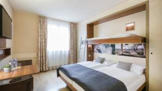 Sie sehen zwei Betten mit Tagesdecke im Familienzimmer FF3 im JUFA Hotel Graz City***. Der Ort für erlebnisreichen Städtetrip für die ganze Familie und der ideale Platz für Ihr Seminar.