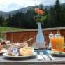 Sie sehen einen gedeckten Brunch-Tisch mit Gebäck, Marmelade, Saft auf der Terrasse vom JUFA Hotel Malbun – Alpin-Resort*** mit Bergblick. Der Ort für erholsamen Familienurlaub und einen unvergesslichen Wanderurlaub.