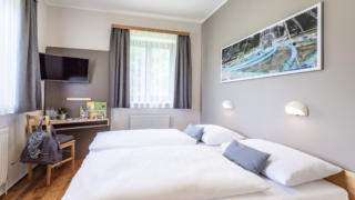 Sie sehen ein Doppelbett in einem Appartement Typ 4 im JUFA Hotel Maria Lankowitz mit TV. JUFA Hotels bietet tollen Sommerurlaub an schönen Seen für die ganze Familie.