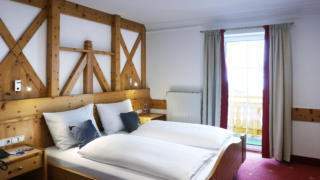Sie sehen ein Doppelbett in einem Doppelzimmer im JUFA Alpenhotel Saalbach**** mit Balkonfenster. JUFA Hotels bietet erholsamen Familienurlaub und einen unvergesslichen Winterurlaub.