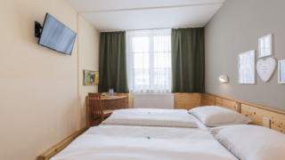 Sie sehen ein Doppelbett in einem Doppelzimmer im JUFA Hotel Bad Aussee*** mit TV. JUFA Hotels bietet erholsamen Familienurlaub und einen unvergesslichen Winter- und Wanderurlaub.