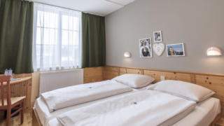 Sie sehen ein Doppelbett in einem Doppelzimmer im JUFA Hotel Bad Aussee*** mit Wandbildern. JUFA Hotels bietet erholsamen Familienurlaub und einen unvergesslichen Winter- und Wanderurlaub.