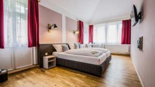 Sie sehen ein Doppelbett in einem Doppelzimmer im JUFA Hotel Königswinter/Bonn mit Fernseher. JUFA Hotels bietet erlebnisreichen Städtetrip für die ganze Familie und den idealen Platz für Ihr Seminar.