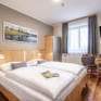 Sie sehen ein Doppelbett in einem Doppelzimmer im JUFA Hotel Maria Lankowitz mit Wandbild. JUFA Hotels bietet tollen Sommerurlaub an schönen Seen für die ganze Familie.