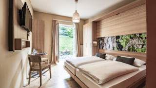 Sie sehen ein Doppelbett in einem Doppelzimmer im JUFA Hotel Murau mit Terrasse. JUFA Hotels bietet erholsamen Familienurlaub und einen unvergesslichen Winter- und Wanderurlaub.