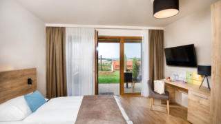 Sie sehen ein Doppelbett in einem Doppelzimmer Plus im JUFA Hotel Neutal – Landerlebnis mit Terrasse. JUFA Hotels bietet Ihnen den Ort für erlebnisreichen Natururlaub für die ganze Familie.