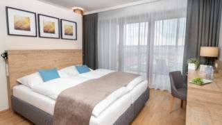 Sie sehen ein Doppelbett in einem Doppelzimmer Plus im JUFA Hotel Neutal – Landerlebnis mit Tisch. JUFA Hotels bietet Ihnen den Ort für erlebnisreichen Natururlaub für die ganze Familie.