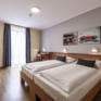 Sie sehen ein Doppelbett in einem Doppelzimmer im JUFA Hotel Seckau mit Wandbildern. JUFA Hotels bietet erholsamen Familienurlaub und einen unvergesslichen Winter- und Wanderurlaub.