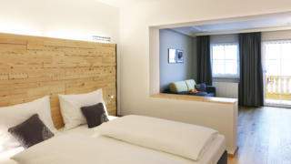 Sie sehen ein Doppelbett in einem Doppelzimmer Superior im JUFA Alpenhotel Saalbach**** mit Balkon. JUFA Hotels bietet erholsamen Familienurlaub und einen unvergesslichen Winterurlaub.