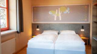 Sie sehen ein Doppelbett im Familienzimmer FF3 Suite im JUFA Hotel Mariazell – Sigmundsberg. Der Ort für erholsamen Familienurlaub und einen unvergesslichen Winter- und Wanderurlaub.
