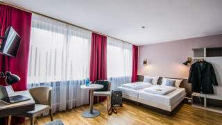 Sie sehen ein Doppelbett in einem Familienzimmer Typ Family and Friends 3 im JUFA Hotel Königswinter/Bonn mit Tisch. JUFA Hotels bietet erlebnisreichen Städtetrip für die ganze Familie und den idealen Platz für Ihr Seminar.