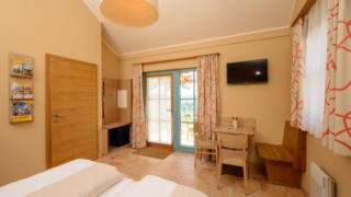 Sie sehen ein Doppelbett in einem Sommerhaus im JUFA Hotel Neutal – Landerlebnis***/**** mit einer Sitzecke. JUFA Hotels bietet Ihnen den Ort für erlebnisreichen Natururlaub für die ganze Familie.