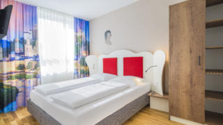 Sie sehen ein Doppelbett in einer Suite4 mit Couch im JUFA Hotel Salzburg City. Der Ort für erholsamen Familienurlaub und einen unvergesslichen Winter- und Wanderurlaub.