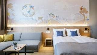 Sie sehen ein Doppelzimmer mit Couch und Bett im JUFA Hotel Weiz. Der Ort für kinderfreundlichen und erlebnisreichen Urlaub für die ganze Familie.