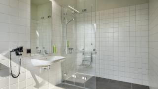 Sie sehen ein Badezimmer eines Doppelzimmer deluxe im JUFA Hotel Bregenz am Bodensee mit Waschbecken und barrierefreier Dusche. Der Ort für einen unvergesslichen Wander-, Rad- und Kultururlaub für Familien, Freunde und Paare.