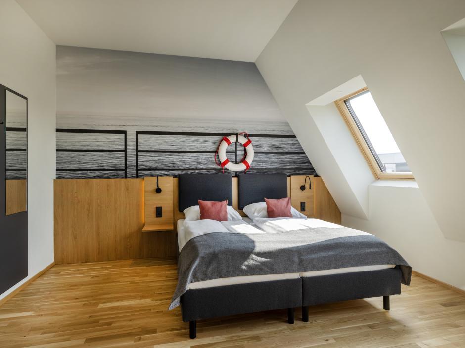 Sie sehen ein Doppelbett vor einer Fototapete in einem Doppelzimmer deluxe im JUFA Hotel Bregenz am Bodensee. Der Ort für einen unvergesslichen Wander-, Rad- und Kultururlaub für Familien, Freunde und Paare.