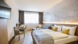 Sie sehen ein Doppelzimmer mit Doppelbett im JUFA Hotel Weiz. Der Ort für kinderfreundlichen und erlebnisreichen Urlaub für die ganze Familie.