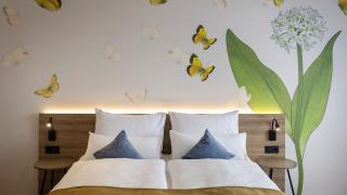 Sie sehen ein Doppelzimmer für zwei Personen im JUFA Hotel Bad Radkersburg mit komfortablem Boxpringbett, modernem Möbiliar und kreativer Wanddeko.