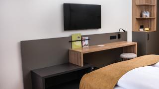 Sie sehen ein Sideboard mit TV, Schreibtisch und Kasten in einem Doppelzimmer im JUFA Hotel Bad Radkersburg.