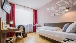 Sie sehen ein Einzelbett in einem Einzelzimmer im JUFA Hotel Königswinter/Bonn mit TV. JUFA Hotels bietet erlebnisreichen Städtetrip für die ganze Familie und den idealen Platz für Ihr Seminar.
