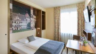 Sie sehen ein Einzelzimmer mit Bett und Tagesdecke im JUFA Hotel Graz City***. Der Ort für erlebnisreichen Städtetrip für die ganze Familie und der ideale Platz für Ihr Seminar.