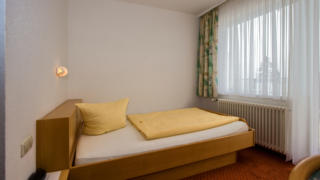Sie sehen ein Einzelbett im Einzelzimmer im JUFA Hotel Schwarzwald. Der Ort für erholsamen Familienurlaub und einen unvergesslichen Winter- und Wanderurlaub.