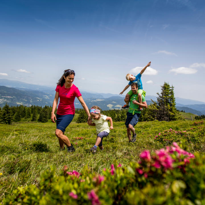Sie sehen eine Familie auf dem Kreischberg im Murtal mit Blumen im Sommer. JUFA Hotels bietet erholsamen Familienurlaub und einen unvergesslichen Winter- und Wanderurlaub.