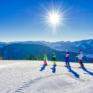 Sie sehen eine Familie beim Skifahren mit Sonne und Bergen auf der Mariazeller Bürgeralpe. JUFA Hotels bietet erholsamen Familienurlaub und einen unvergesslichen Winterurlaub.