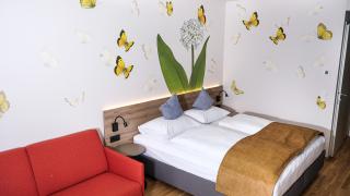 Sie sehen ein Family & Friends 4 Zimmer im neuen JUFA Hotel Bad Radkersburg mit komfortablen Boxspringbett, Wanddeko und ausziehbarer Schlafcouch.